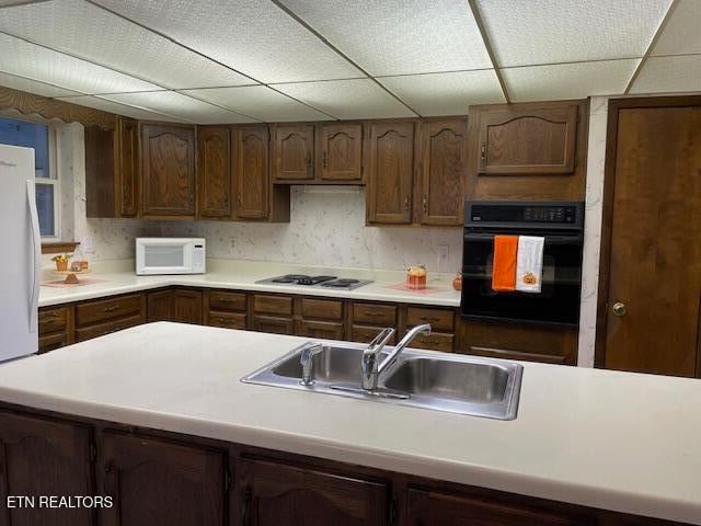 kitchen featuring dark brown cabinetry, white appliances, a drop ceiling, and sink