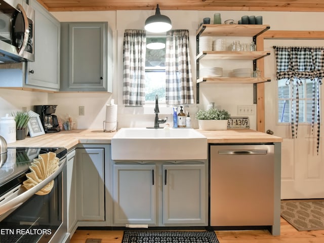 kitchen with hanging light fixtures, light hardwood / wood-style flooring, sink, gray cabinets, and stainless steel appliances