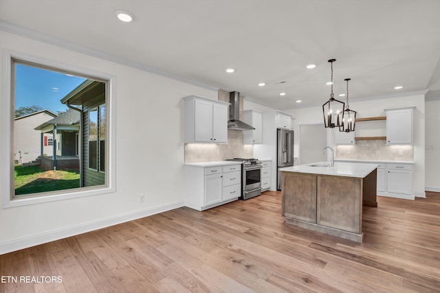 kitchen with an island with sink, white cabinetry, stainless steel appliances, wall chimney exhaust hood, and decorative light fixtures