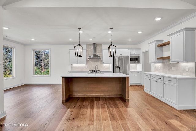 kitchen featuring wall chimney exhaust hood, appliances with stainless steel finishes, hanging light fixtures, and light hardwood / wood-style flooring