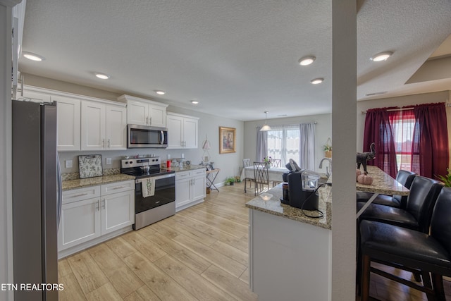 kitchen with appliances with stainless steel finishes, light stone counters, white cabinets, and light hardwood / wood-style floors