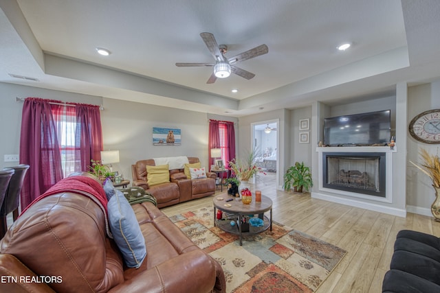 living room featuring light hardwood / wood-style flooring, a tray ceiling, and ceiling fan