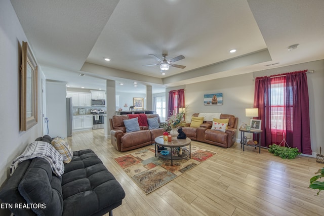 living room with a tray ceiling, light wood-type flooring, and ceiling fan