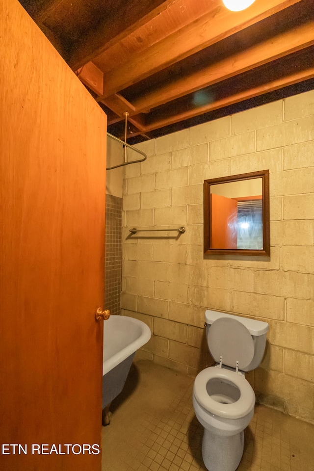 bathroom with a tub to relax in, beamed ceiling, toilet, and tile patterned floors