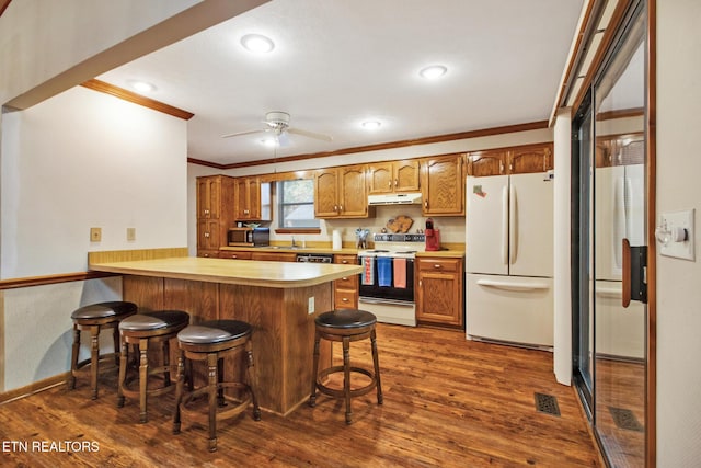 kitchen featuring white appliances, dark hardwood / wood-style flooring, ornamental molding, a kitchen bar, and kitchen peninsula