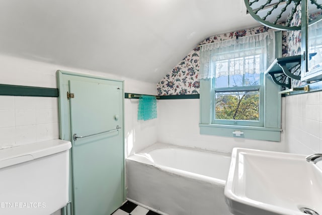 bathroom with sink, a tub to relax in, tile walls, and vaulted ceiling