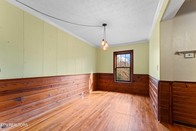 empty room featuring wood walls, wood-type flooring, ornamental molding, and a textured ceiling