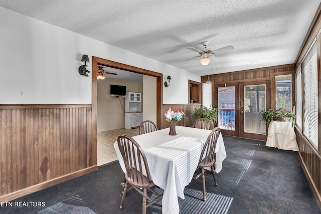 carpeted dining room featuring french doors, ceiling fan, a textured ceiling, and wooden walls