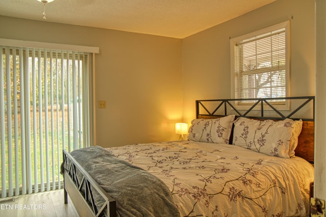 bedroom with light hardwood / wood-style flooring, a textured ceiling, and access to outside