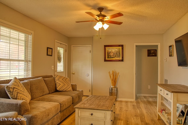 living room with a textured ceiling, light wood-type flooring, and ceiling fan