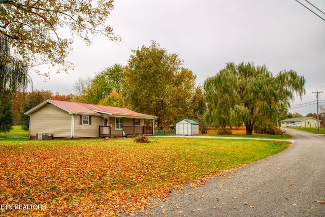 view of front of home featuring covered porch, a storage shed, and a front lawn