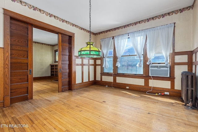 unfurnished dining area featuring cooling unit, radiator heating unit, and light wood-type flooring