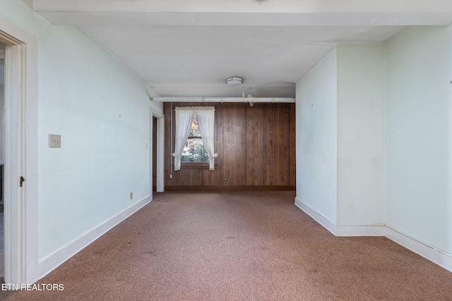 carpeted spare room featuring beam ceiling and wood walls