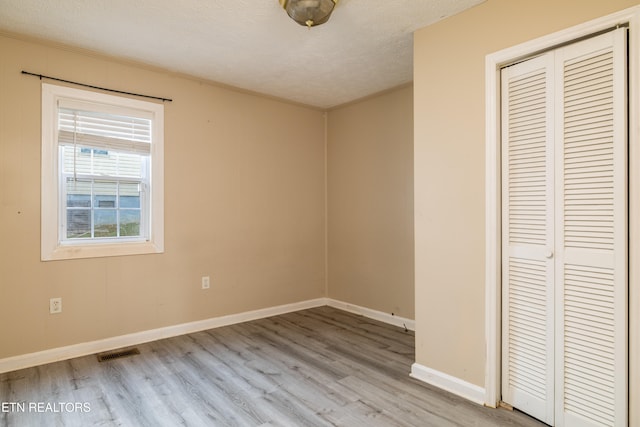 unfurnished bedroom with light hardwood / wood-style flooring, a textured ceiling, and a closet