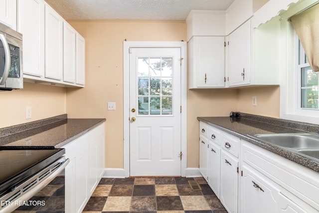 kitchen with appliances with stainless steel finishes, white cabinetry, a textured ceiling, and a healthy amount of sunlight