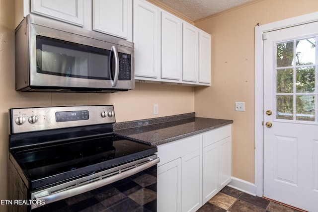 kitchen with appliances with stainless steel finishes, a textured ceiling, white cabinetry, and dark stone countertops