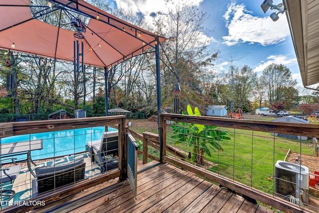 deck with a pool, a storage shed, cooling unit, and a lawn