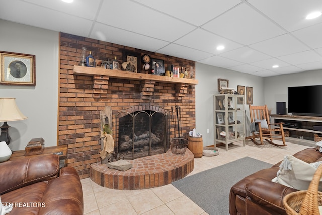 living room with light tile patterned flooring, a drop ceiling, and a brick fireplace