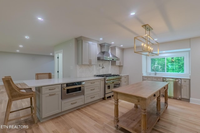 kitchen featuring appliances with stainless steel finishes, wall chimney range hood, light countertops, light wood-style floors, and recessed lighting