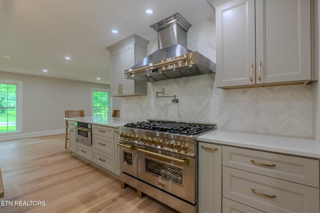 kitchen featuring appliances with stainless steel finishes, wall chimney exhaust hood, decorative backsplash, light wood-style floors, and light countertops