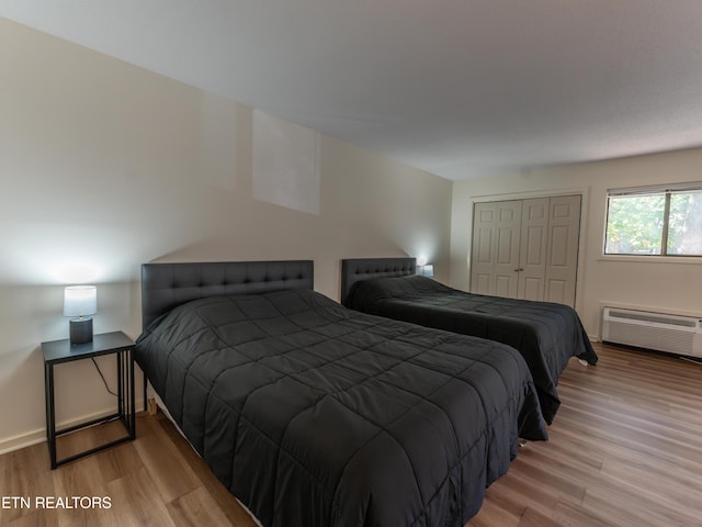 bedroom with light hardwood / wood-style floors, a wall unit AC, and a closet