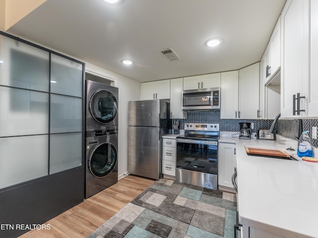 kitchen featuring appliances with stainless steel finishes, backsplash, light hardwood / wood-style floors, white cabinets, and stacked washer / drying machine