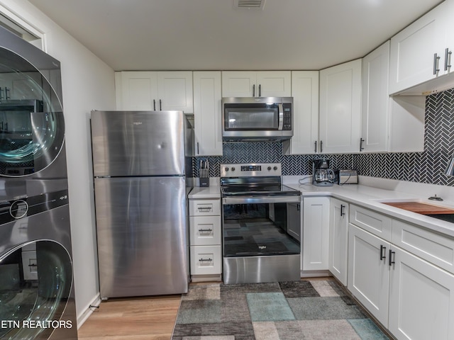 kitchen with white cabinets, tasteful backsplash, stacked washing maching and dryer, light wood-type flooring, and stainless steel appliances