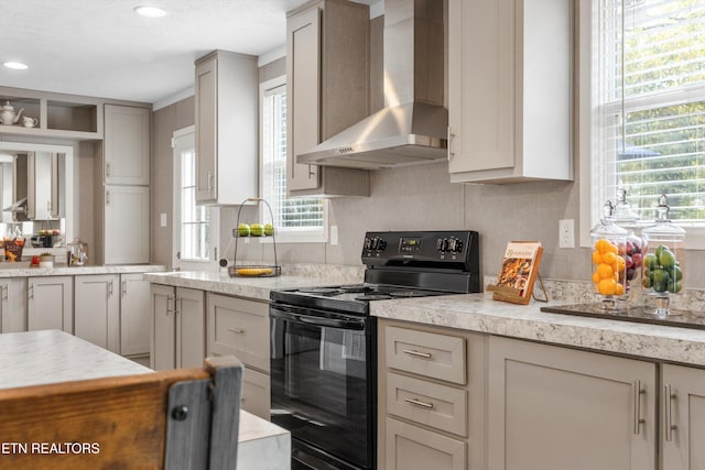 kitchen featuring black electric range, light stone counters, and wall chimney exhaust hood