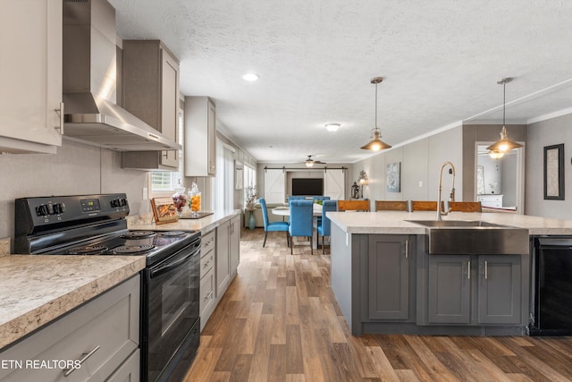 kitchen featuring wall chimney range hood, hanging light fixtures, gray cabinetry, black appliances, and dark hardwood / wood-style flooring