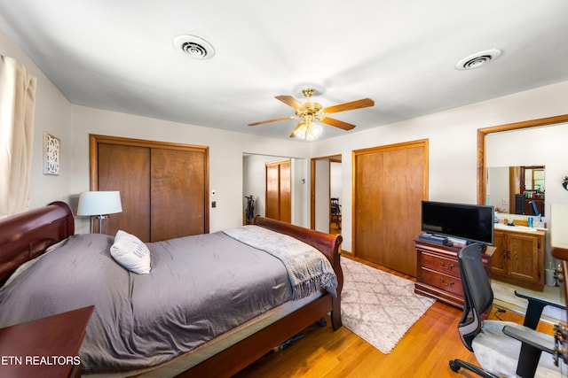 bedroom featuring ceiling fan, light hardwood / wood-style flooring, and multiple closets