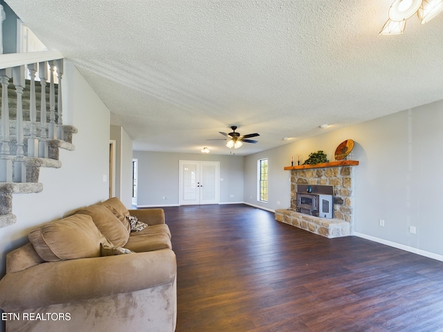 living room featuring ceiling fan, a textured ceiling, dark hardwood / wood-style flooring, and a wood stove