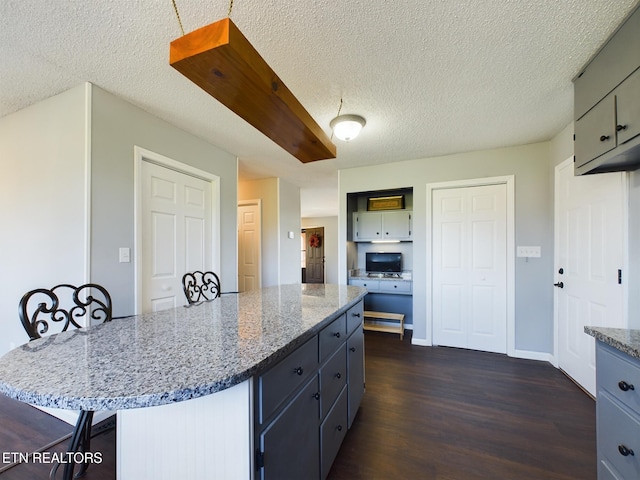 kitchen with a breakfast bar area, a center island, light stone countertops, gray cabinets, and dark hardwood / wood-style flooring