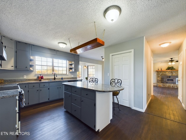 kitchen with ceiling fan, a textured ceiling, a center island, and dark hardwood / wood-style flooring