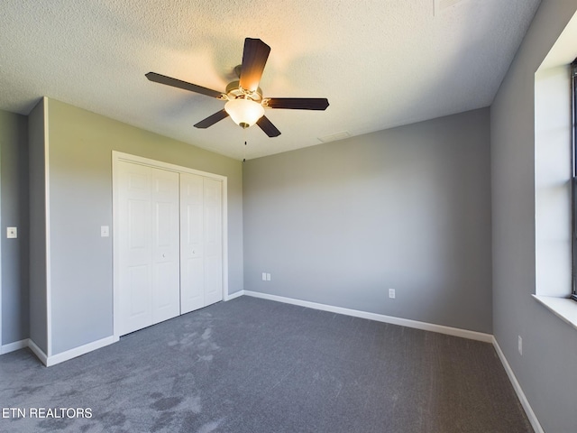 unfurnished bedroom featuring a closet, a textured ceiling, dark carpet, and ceiling fan