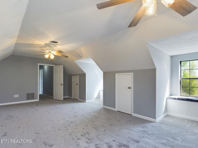 bonus room with lofted ceiling, a textured ceiling, light colored carpet, and ceiling fan