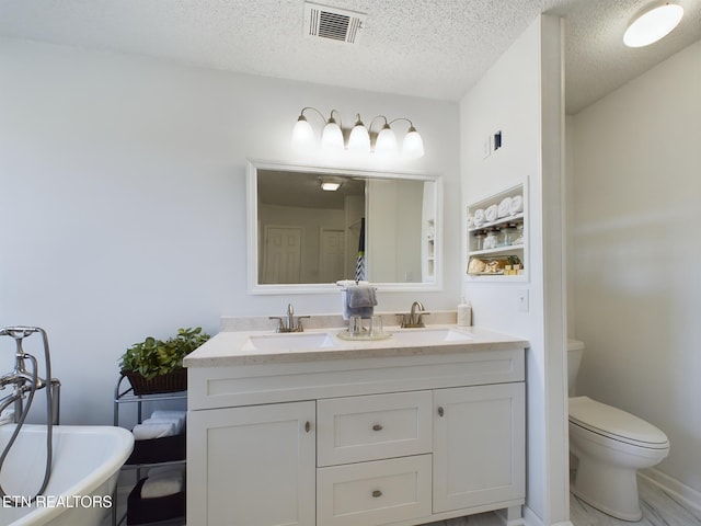 bathroom with vanity, toilet, a tub to relax in, and a textured ceiling