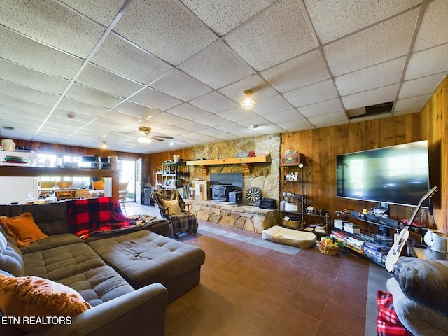 living room with wooden walls, a paneled ceiling, a wood stove, and ceiling fan