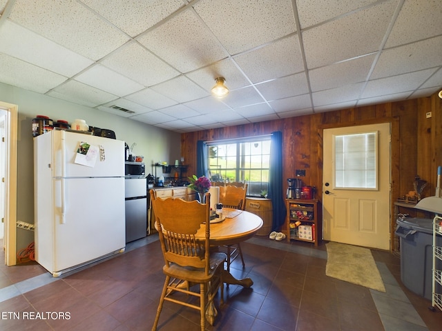 dining space featuring a drop ceiling and wooden walls