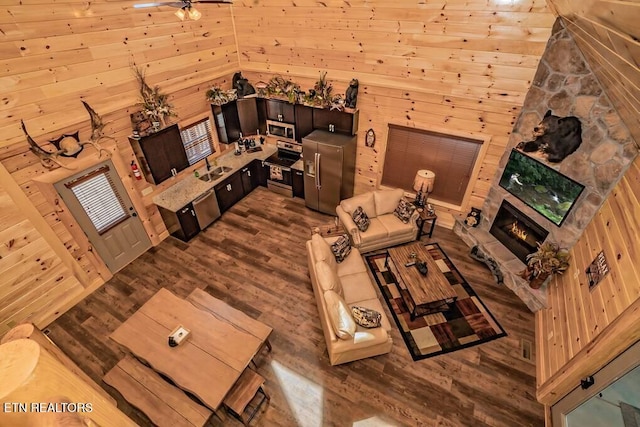 living room featuring ceiling fan, wood walls, dark hardwood / wood-style flooring, and a stone fireplace