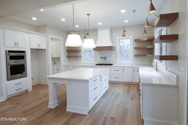 kitchen with stainless steel double oven, a center island, premium range hood, and white cabinetry