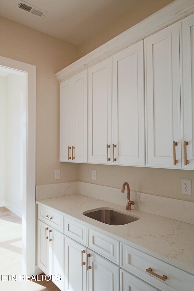 kitchen featuring white cabinets, light stone counters, and sink