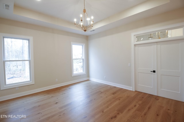 unfurnished room with an inviting chandelier, light wood-type flooring, and a tray ceiling