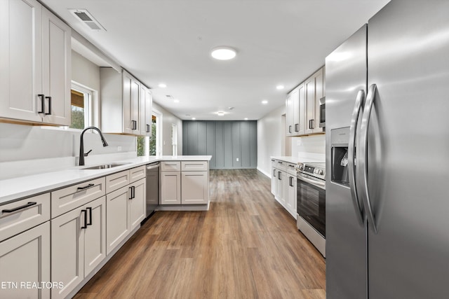 kitchen with white cabinetry, sink, stainless steel appliances, kitchen peninsula, and hardwood / wood-style floors