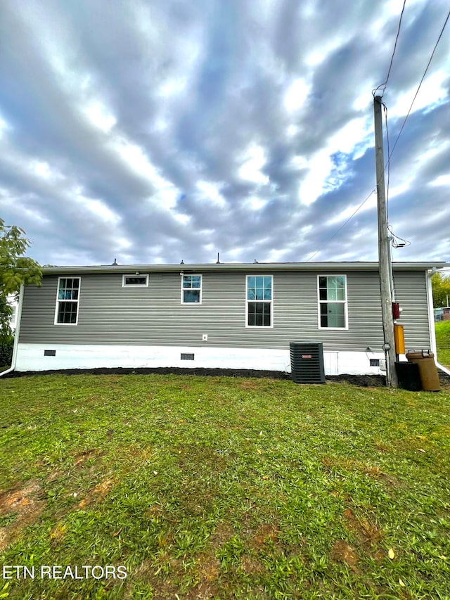 rear view of property with central AC unit and a lawn