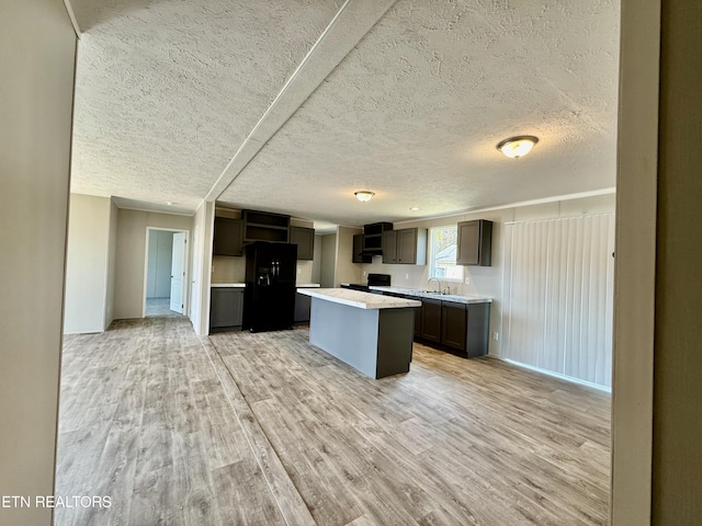 kitchen with a center island, light countertops, black refrigerator with ice dispenser, light wood-type flooring, and a sink