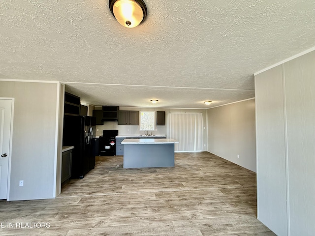 kitchen with a center island, light countertops, black fridge with ice dispenser, and light wood finished floors