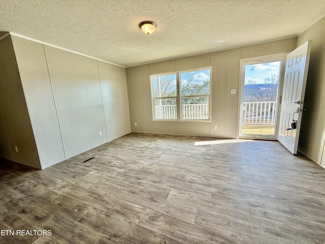 empty room with visible vents, a textured ceiling, and wood finished floors