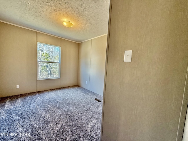 spare room featuring a textured ceiling, ornamental molding, carpet flooring, and visible vents