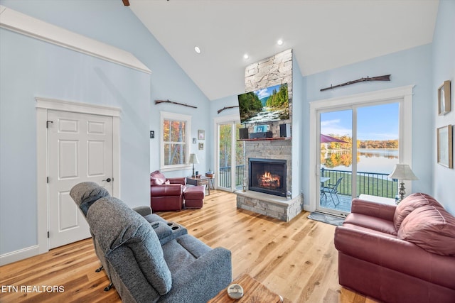 living room with high vaulted ceiling, a stone fireplace, and hardwood / wood-style floors