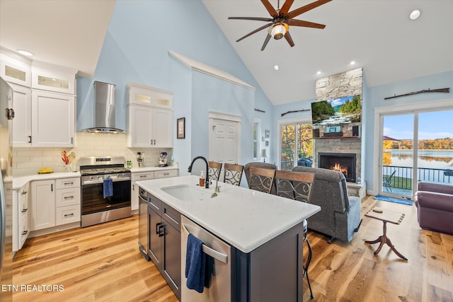 kitchen featuring a center island with sink, appliances with stainless steel finishes, wall chimney range hood, and white cabinetry